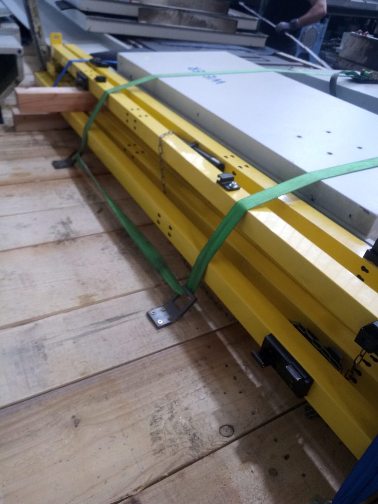 Maschinenbauteile mit Spannbändern an verschraubten Befestigungslaschen auf einer Transportpalette gesichert